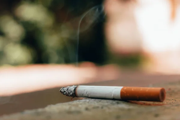 城市里 白色点燃的香烟 混凝土地板上坐着橙色的过滤器 危险和有毒的习惯 可能导致不同的疾病 并使生命处于危险之中 — 图库照片