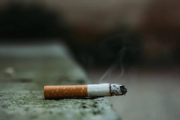 略带橙色滤嘴的白色香烟 冒出浓烟 坐在灰色的城市混凝土上 有抄袭的空间 导致多种疾病的危险和有毒的习惯 — 图库照片