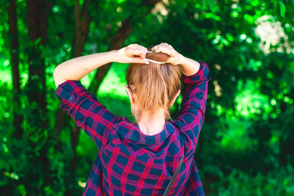 若い女性は彼女の短い茶色の髪の屋外を結ぶ カジュアルな服装ティーンアレンジ彼女の髪型で自然上の緑の背景 — ストック写真