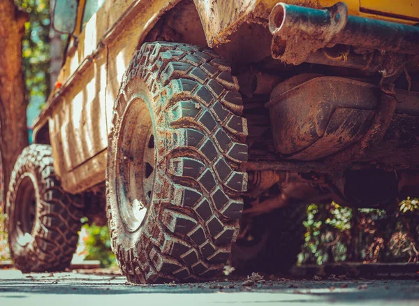 Big and dirty tires of an off-road car sitting on the street. Yellow monster truck with huge rubber wheels with a rough and detailed surface