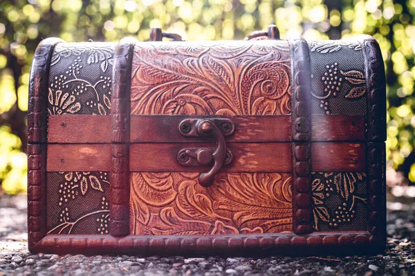 Wooden mystery box with fine beautiful carvings and decorations placed on the ground in nature with a blurred background. Small chest for storing jewelry