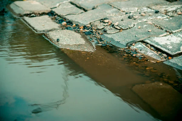 街の通りに泥だらけの水たまりの石の境界付近の大きな穴に集まった 大規模な雨の後の都市インフラの問題 — ストック写真