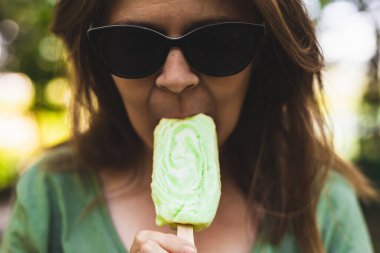 Dondurmadan bir ısırık alan kız. Güneş gözlüklü genç yaz sıcağında buzlu çöl yiyor.