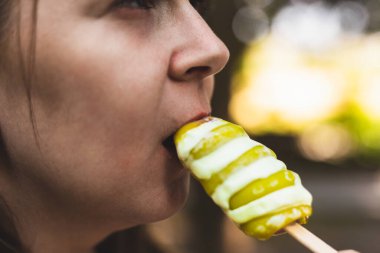Sarmal şekilli dondurmadan bir ısırık alan bir kızı yakından çek. Genç yaz sıcağında buzlu, yuvarlak bir çöl yiyor.