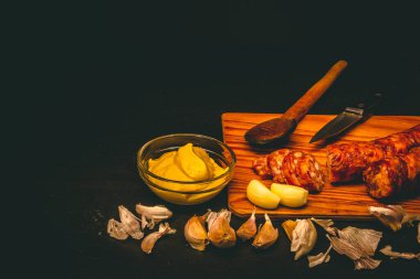 Çiğ domuz eti sosisi tarifi ve malzemeler. Kabuklu sarımsak, çatal bıçak takımı ve pişmemiş sosislerden yapılmış koyu kırsal ve geleneksel yemek arkaplanı.