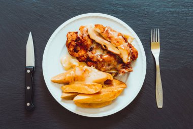 Cordon bleu ve patates tablosunun en üst görüntüsü. Koyu gıda arka planında ardesia taşı var.