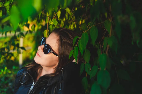 Happy young blind woman with black sunglasses sitting in the bright sun outdoor. Smiling and joyful girl with visual disability relaxing in nature