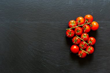 Sağ tarafta kırmızı kiraz domatesleri, siyah taşlı arka planda. Sağlıklı yaşam tarzı için vitamin dolu taze organik sebzeler.