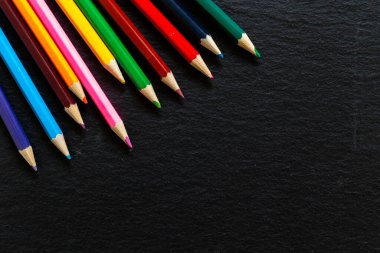 Siyah arka planda sol köşede renkli keskin kalemler var. Koyu taş desenli yüzeyde çizim araçları. Eğitim için resim kavramı