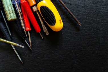 Evin sol köşesine siyah arka planda çalışma aletleri yerleştirilmiş. Koyu renkli taş desenli yüzeyde metal ve plastik onarım seti