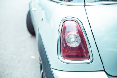 Park halindeki küçük bir arabanın stop lambaları. Sol tarafında yakıt kapısı olan küçük bir aracın arka görüntüsü park alanında duruyor.