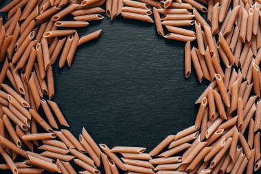 Yaratıcı makarna arka planı. Koyu renkli bir makarna yığınının ortasında siyah desenli bir levhada duran bir çember.