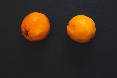 İki büyük portakal, fotokopi alanı olan karanlık bir taş tahtanın üstüne yerleştirilmiş. Siyah arka planda taze tropikal tatlı ve sulu meyveler