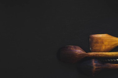 Siyah arka planda tahta mutfak aletleri ve fotokopi alanı. Koyu dokulu yüzeyde eski ve kullanılmış kırsal aletler