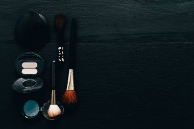Siyah arka planın sol tarafında gözlük ve fırçalar var. Minimalist düz yüzeyde kozmetik ürünler vardı. Kadın güzelliği için imaj kavramı