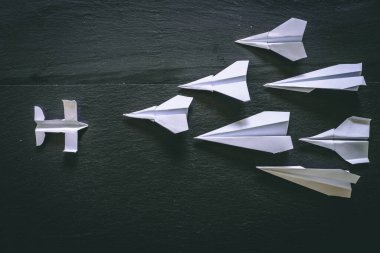 Bir origami kağıt uçak, siyah arka planda diğer kağıt uçaklardan oluşan bir grupla karşı karşıya. Liderlik ve yaratıcılık için imajı kavra