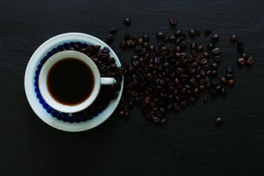 Siyah arka planda izole edilmiş kavrulmuş kahve çekirdekleri dışında. Kahvaltı içeceği ve kahve çekirdekli mavi kahve tabağı..