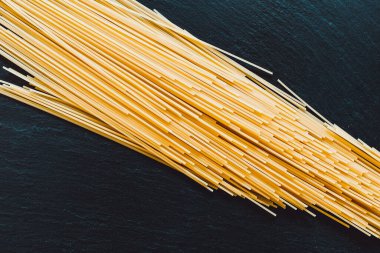 Uzun ve ince sarı bir spagetti siyah bir arkaplana çapraz yerleştirilmiş. İtalyan makarnası çeşitli tariflerde kullanılır.