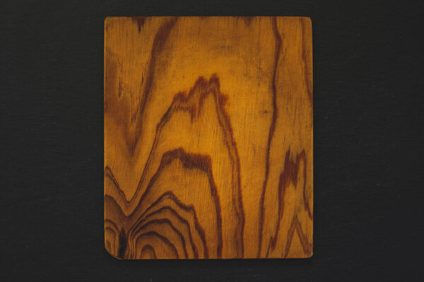 Square wooden cutting board on black background. Textured timber plank used for cutting foods. Rustic handmade kitchen equipment