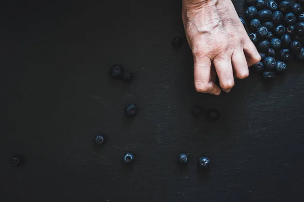 Top view of hand grabbing small blueberries placed on a black background. Healthy and sweet fruits full of vitamins and antioxidants