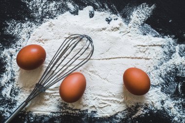 Siyah arka planda tam yumurtalı beyaz un ve metalik çırpı. Temel hamur malzemeleri ve fırınlarda kullanılan aletler. Sağlıklı yemek pişirme imajı