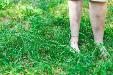 Bir bahar günü parkta çıplak ayakla yürüyen genç bir kadın. Bileklikli kız taze yeşil bir çayırda dinleniyor. Ayak bakımı için resmi kabul et
