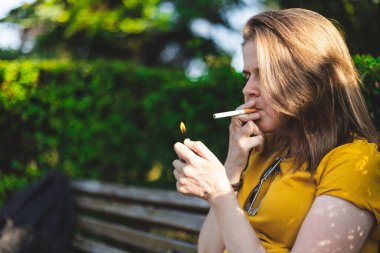 Genç bir kız güneşli bir günde dışarıda sigara yakıyor. Kahverengi saçlı, açık renk ve purolu güzel bir kız. Nikotin bağımlılığıyla gelişigüzel giyinmiş milenyum.