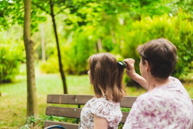 Anne, kızının uzun kahverengi saçlarını dışarıda tarıyor. Genç kız ve kıdemli kadın parkta birlikte eğleniyorlar. Aile ve yaşam tarzı için kavramsal görüntü