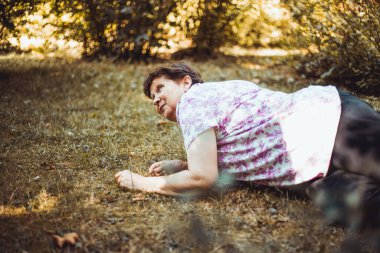 Dışarıda yerde yatan yaşlı bir kadın yaralanmış. Çimenlerde kayıp düştükten sonra dirsekleri ve dizleri üzerinde oturan yaralı yaşlı kadın. Zayıf yaşlı kişi küçük bir kaza geçirdi.