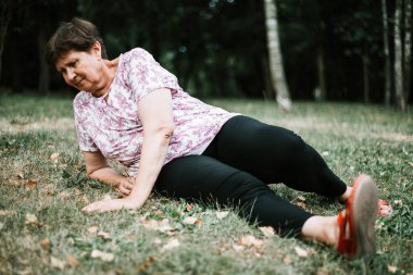 Parkta düştükten sonra yerde yatan üzgün ve yaralı yaşlı kadın. Bayıldıktan sonra oturan narin yaşlı kadın. Kalp sorunu olan yaşlı birinin yardıma ihtiyacı var.