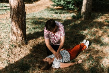 Kıdemli kadın sırt üstü yatan genç bir kıza kalp masajı yapıyor. Kardiyopulmoner canlandırma yardımı