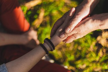 Son sınıf öğrencisinin dışarıda genç birinin elini tutarken çekilmiş yakın plan fotoğrafı. Kız büyükanneye yardım ediyor ve yaşlı insanlar için sevgi ve sevgi dolu bir jest sunuyor.