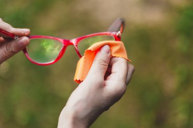 Dışarıda turuncu bezle gözlük temizleyen genç bir adam. Dişi eller açık havada güneşin tozunu alarak pürüzsüz kumaşla göz giysilerini tutar ve temizler.