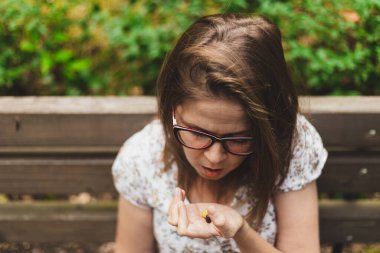 Parktaki bankta oturmuş haplara bakan genç bir kadın. Kahverengi saçlı, gözlüklü, sağlıklı bir yaşam için vitamin ve takviye alan tatlı bir kız.