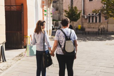 Mutlu anne ve kız güneşli bir günde şehre alışverişe gidiyorlar. Gayri resmi giyinmiş, kahverengi saçlı ve dışarıda el ele tutuşan güzel, yaşlı bir kadın. Eğlenceli ve rahatlatıcı aile aktiviteleri