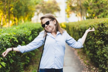 Genç bir kadının dışarıda omzunu kaldırdığından şüpheliyim. Kahverengi saçlı, güneş gözlüğü takan, parkta yürürken bir şeyleri merak eden ve sorgulayan tatlı bir kız.