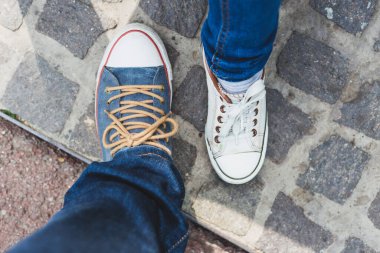 Havalı unisex branda ayakkabılar yan yana duruyor. Kaldırımda duran kızlar ve oğlanlar için beyaz ve mavi spor ayakkabılı ayaklar