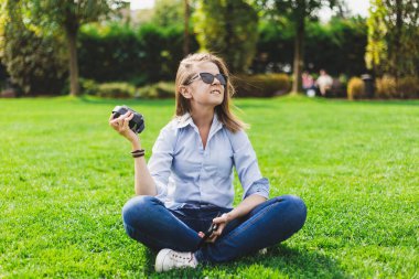 Kız dışarıda otururken portatif hoparlör dinliyor. Millennial, küçük kablosuz giriş cihazıyla parkta eğleniyor. Doğada teknoloji kullanan sevimli bir kadın.