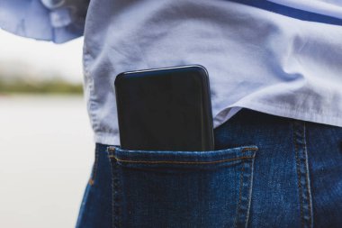 Pantolonun arka tarafındaki akıllı telefon. Kocaman bir cep telefonunun arkasında, dar bir cebin içinde.