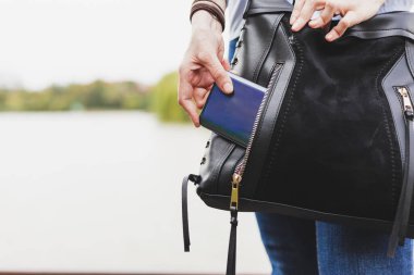 Kot pantolonlu bir kadın, cep telefonunu deri bir çantanın cebinden çıkarıyor. Kot pantolon giymiş bir kadın telefon açmaya çalışıyor.