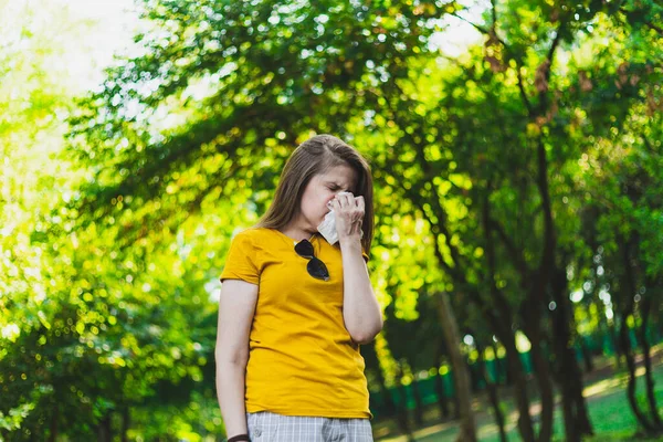 女人在外面打喷嚏穿着黄色T恤的女孩在大自然中间被树木环绕时过敏 — 图库照片