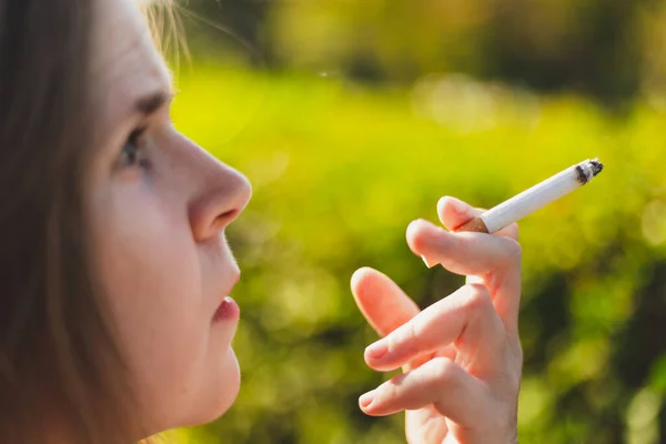 拍摄年轻女子在外面吸烟的特写镜头 在公园里拿着一支点燃的雪茄的漂亮姑娘 有着危险和有毒的习惯 — 图库照片