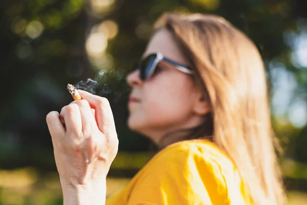 夏天的一天 一个少女在外面抽烟 戴夏季眼镜的年轻女子有危险和有毒的习惯 成瘾的概念形象 — 图库照片