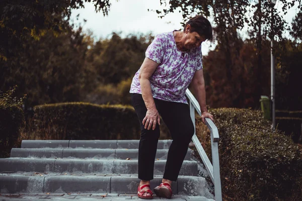 外の階段を歩いている間に 弱い先輩女性が落下しようとしています 公園でかわいいおばあちゃんが滑ります 高齢女性の白い足の痛みと筋肉の不快感 — ストック写真