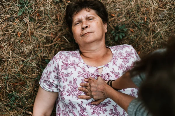 公園に横になって高齢女性にCprを実行する人 若い女性は外の心臓の問題に苦しんでいる老婦人に応急処置を与える 地面に倒れた病人 — ストック写真