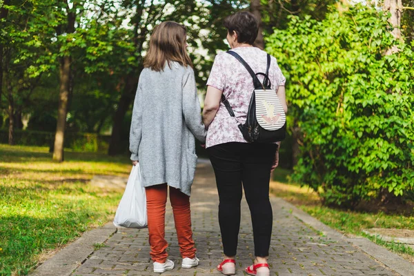 公園を歩いている間 母親が袋を運ぶのを手伝っている娘 時折服を着た女の子の手の皮膚の女性屋外でチャット 他人を助けるためのコンセプトイメージ — ストック写真