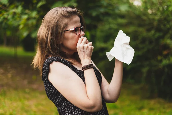 Attractive lady with leaking nose as flu symptoms using a nasal spray medicine with tissue in her hand, allergy or common cold treatments