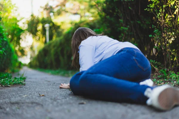 Fainting woman lying on the ground while having heart problems outdoors. Lonely young female fallen on the street after feeling sick. Concept image for epilepsy