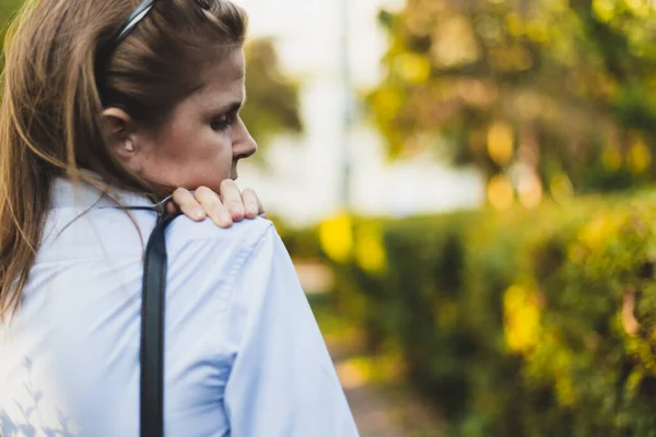 Young woman holding painful shoulder while carrying a heavy purse outdoors. Female worker massaging inflamed joint in the neck. Pretty girl suffering from muscle ache in the back