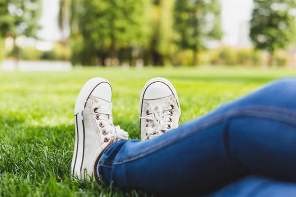 Parktaki çimlerin üzerinde otururken spor ayakkabı ve kot giyen bir adam. Modaya uygun giyimli, bembeyaz ayakkabılı ve kot pantolonlu açık havada rahatlayan bir kız. Şık bir yaz kıyafeti.